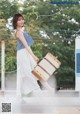 A woman in a blue and white top and white skirt holding a suitcase.