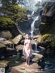 A naked woman standing in front of a waterfall.