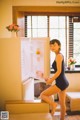 A woman in a black bathing suit standing in front of an open refrigerator.