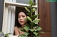 A woman looking out of a window with a plant in front of her.