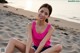 A woman in a pink tank top sitting on a sandy beach.