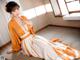 A woman in an orange and white kimono sitting on the floor.